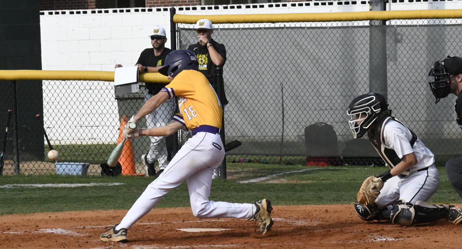 A baseball player in yellow swings at a pitch, with a catcher, umpire, and teammates in the background on a sunny day.