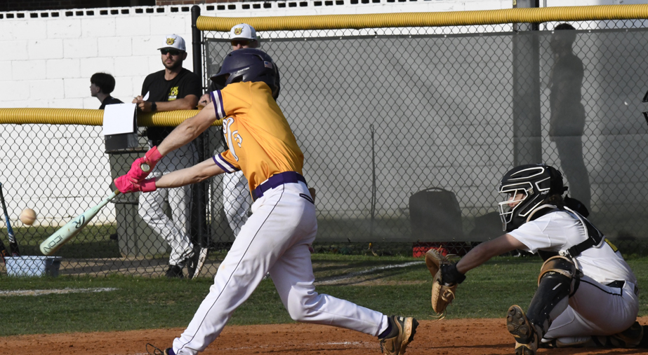 Baseball player in yellow jersey swinging at a pitch, catcher in position, with teammates and fence in the background.