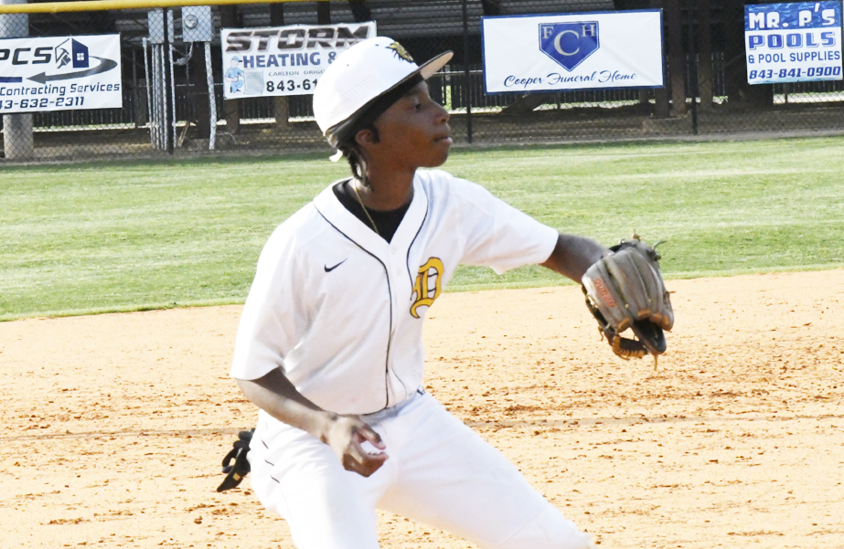 Young baseball player in a white uniform and cap focuses while preparing to catch a ball on a sunny field.