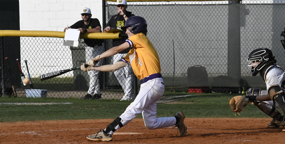 Baseball player in yellow jersey hits a pitched ball while a catcher and teammates watch during a daytime game.