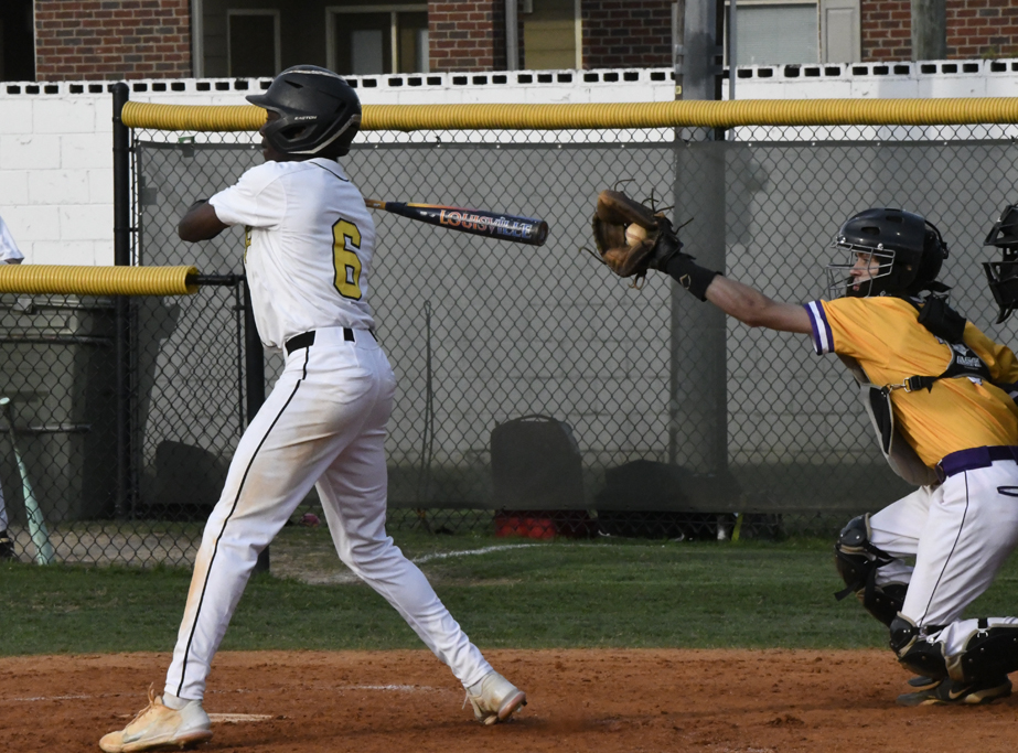 A baseball player in a white uniform swings a bat, while the catcher in yellow gear prepares to catch the ball.