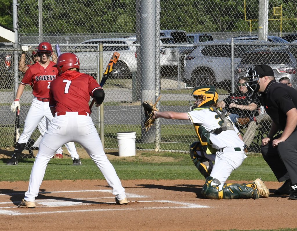 A baseball game moment with a batter in red, a catcher in green and yellow, and an umpire behind home plate, all focusing on the pitch.
