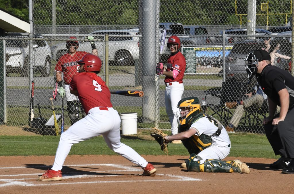 A baseball batter in a red uniform prepares to swing as the catcher and umpire watch closely behind home plate during a game.