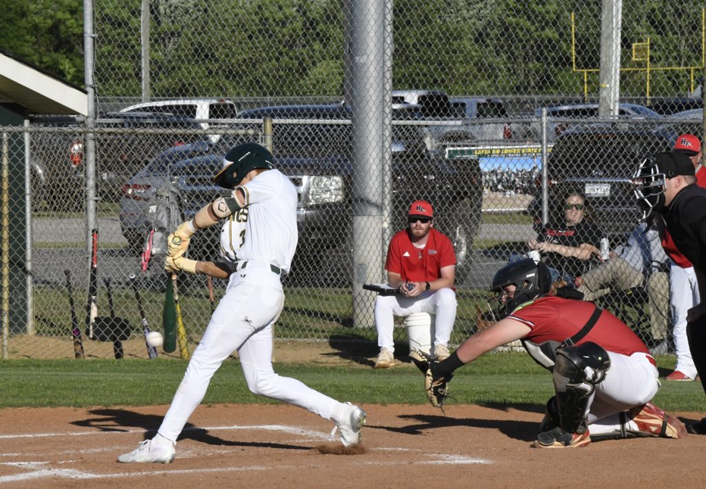 A baseball player in white swings at a pitch as the catcher, umpire, and team members in red observe during a game.