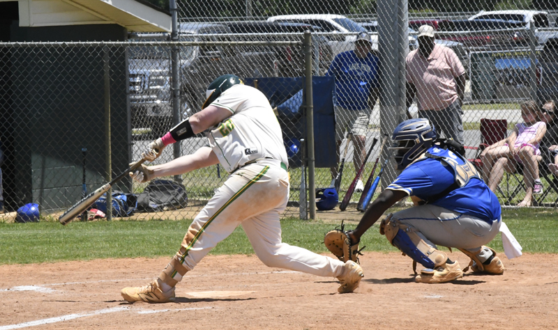 A baseball player in white swings at a pitch while a catcher in blue crouches behind home plate during a daytime game.
