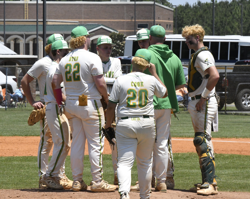 A group of baseball players and a coach huddle on the pitcher's mound during a game on a sunny day.