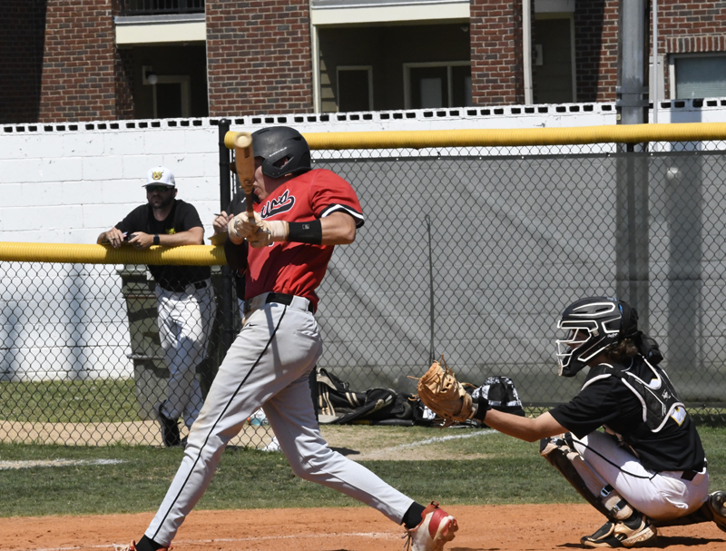 Baseball player in red jersey swinging at a pitch, while the catcher in black gear is ready behind home plate.