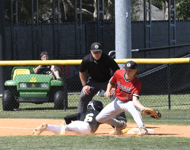 Baseball player slides into base as fielder in red tries to tag, with umpire observing closely and a person sitting in a green vehicle in the background.