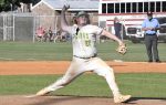 Baseball pitcher in uniform mid-throw on a sunny field, with spectators and an umpire in the background.