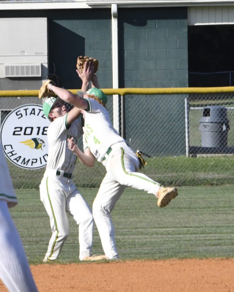 Two baseball players in white uniforms collide while reaching up for a catch on a sunny field.