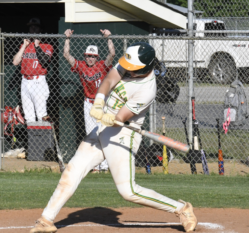 A baseball player in white uniform swings at a pitch, while two players in red uniforms watch from behind a chain-link fence.