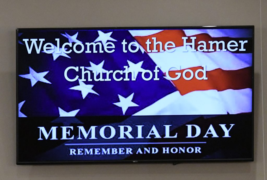 American flag background with text: "Welcome to the Ham Church of God. Memorial Day. Remember and honor." Displayed on a screen.