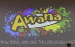 Awana logo with colorful paint splatters in the background and the phrase “Serve, and love the Lord Jesus” below.