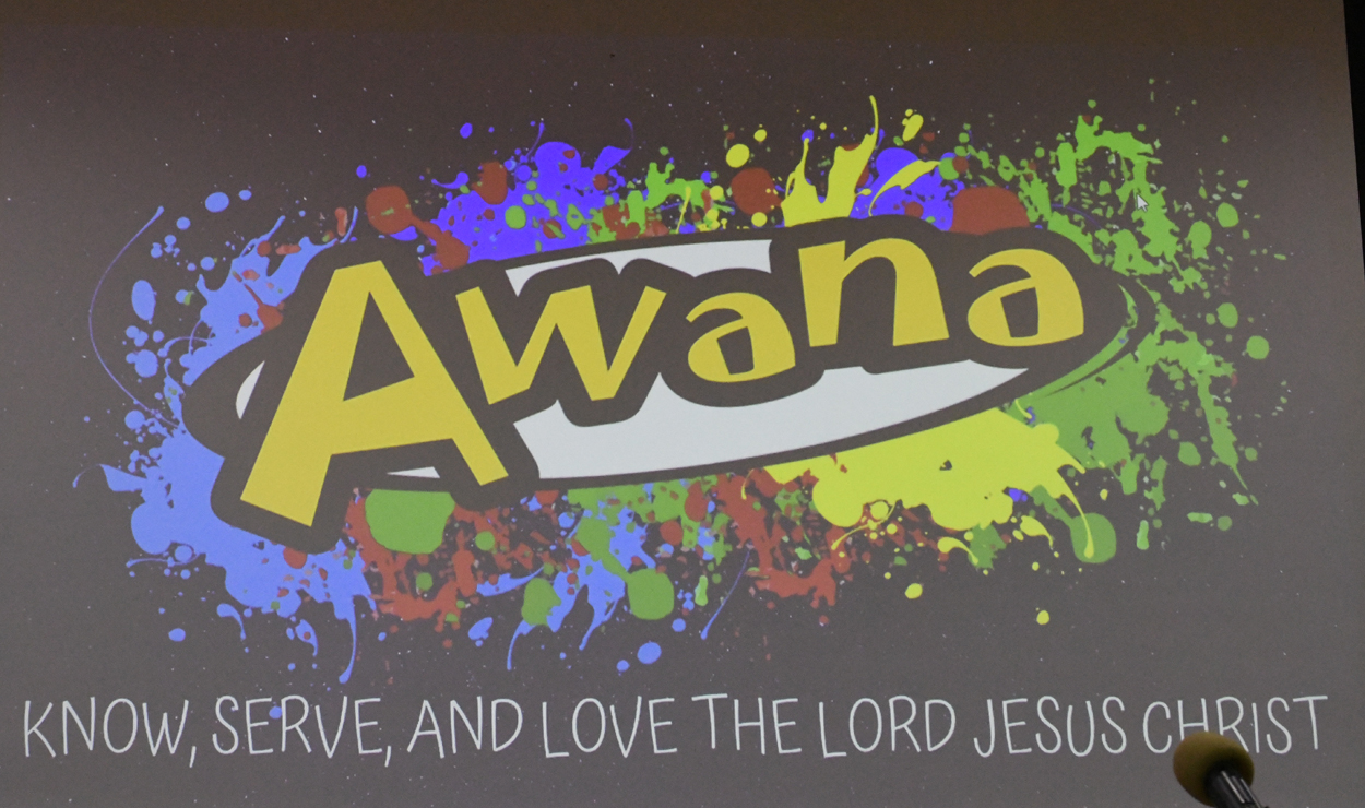 Awana logo with colorful paint splatters in the background and the phrase “Serve, and love the Lord Jesus” below.