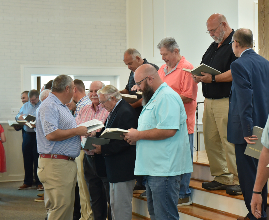 A group of men standing on church steps, holding hymnals or books, appearing to prepare for or participate in a service or choir.