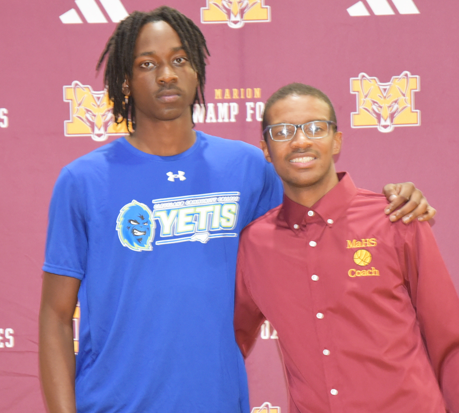 Two men pose together; one wears a blue Yetis shirt, the other a maroon MaHS Coach shirt, standing in front of a maroon Marion Swamp Foxes backdrop.