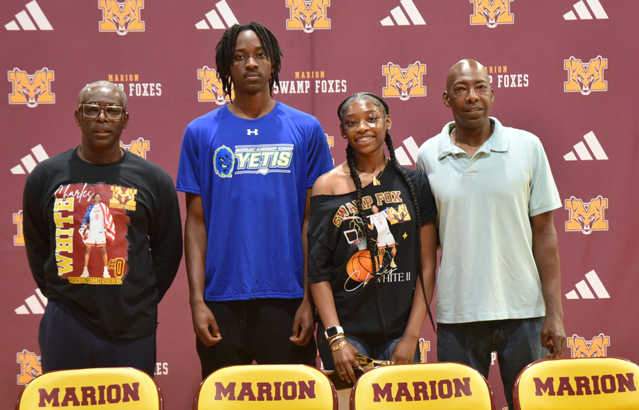 Four people stand together in front of a Marion Swamp Foxes backdrop, posing for a photo with yellow Marion chairs in front of them.