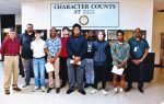 A group of students and staff stand in front of a wall sign reading "Character Counts at DHS" inside a school hallway.