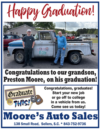 Two people stand in front of a vintage truck. Graduation congratulations to Preston Moore are displayed, with an ad for Moore’s Auto Sales beneath the message.