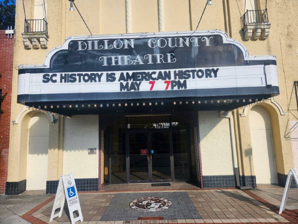 Dillon County Theatre marquee reads "SC History is American History May 7 7PM." Handicap parking sign in front.
