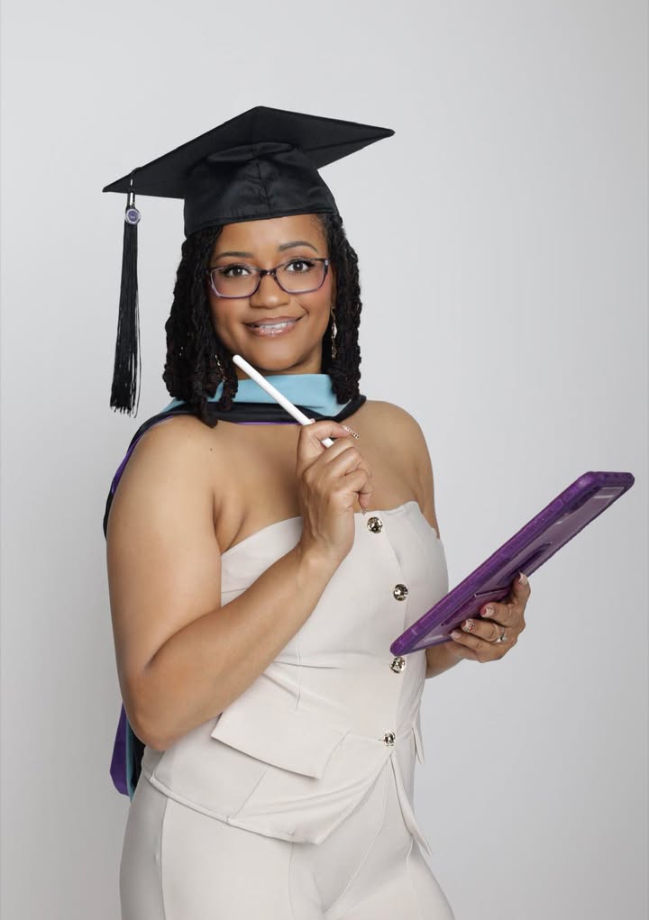 Woman in graduation cap and gown holding a tablet and stylus, smiling at the camera against a plain white background.