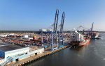 Large cargo ships docked at a busy port with cranes unloading containers and colorful shipping containers stacked along the waterfront.