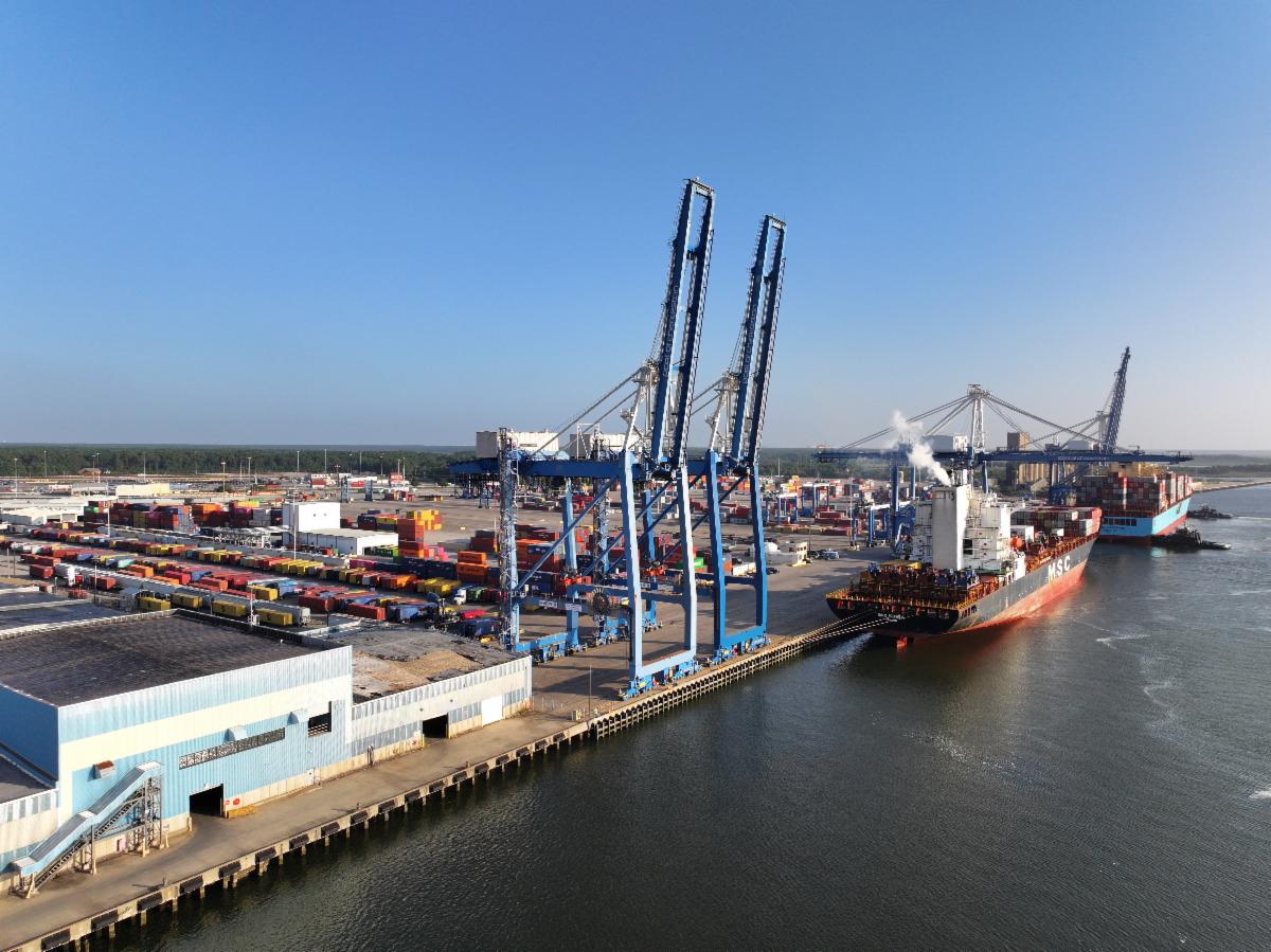 Large cargo ships docked at a busy port with cranes unloading containers and colorful shipping containers stacked along the waterfront.