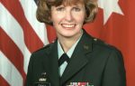 A woman in a military uniform with the name "Frost," standing in front of American and red flags with white star symbols.