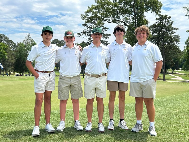 Five teenage boys in white golf shirts and shorts standing together on a golf course, smiling on a sunny day.