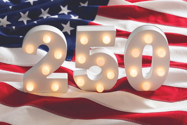 Large illuminated numbers "250" on a wavy American flag background, celebrating the 250th anniversary of the United States.