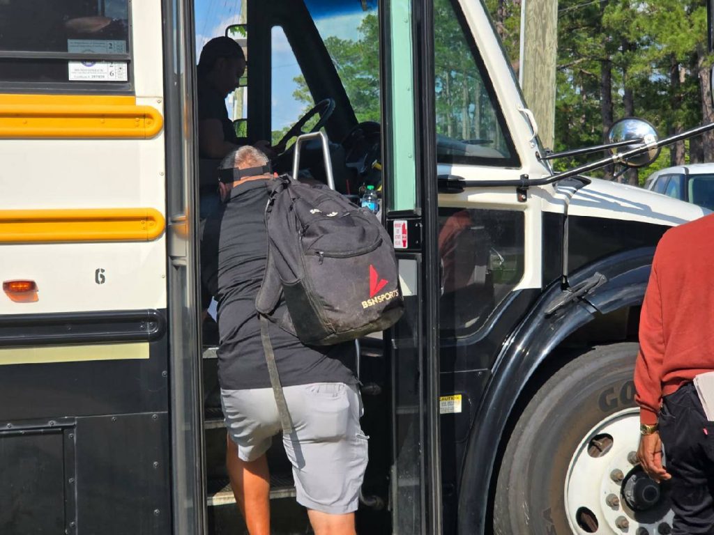 A person with a black backpack board a school bus while another person stands nearby; the driver is visible inside the bus.