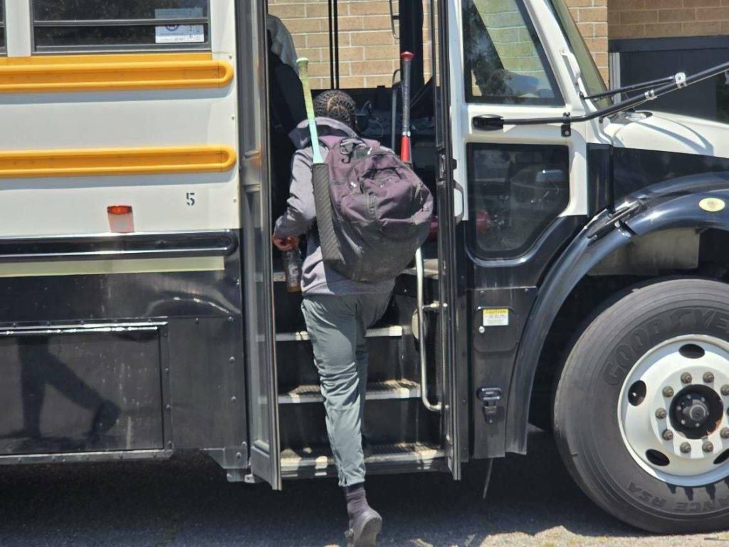 A person with a large backpack and a walking stick is boarding a school bus.