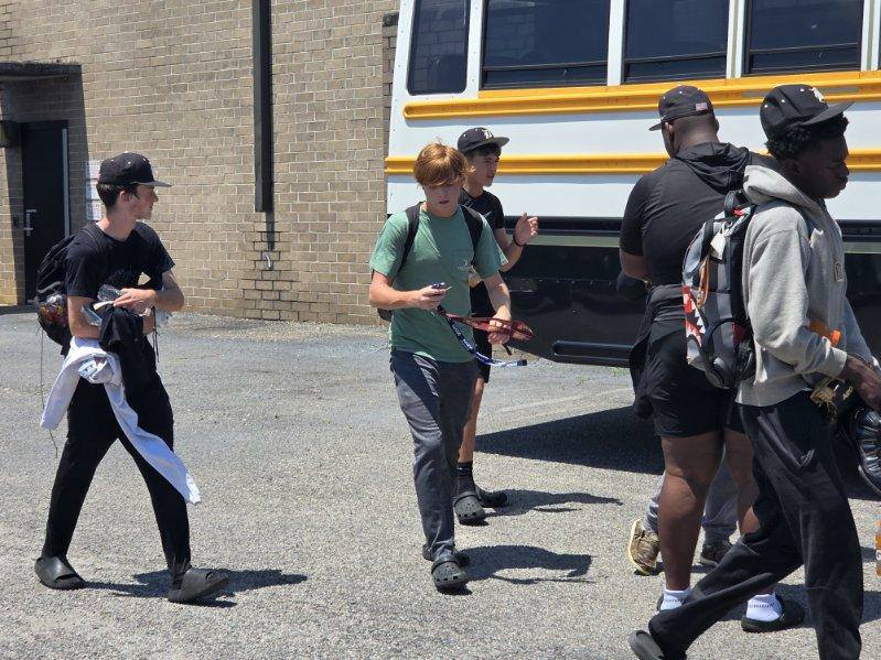 A group of young people with backpacks walking beside a parked yellow and white school bus on a sunny day.
