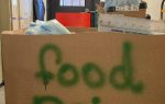 Large cardboard box labeled "food drive," filled with bags and boxes, sits in front of double doors in an indoor hallway.
