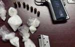 Silver handgun with bullets, magazine, and several small plastic bags containing white powder, all placed on a dark wooden surface.