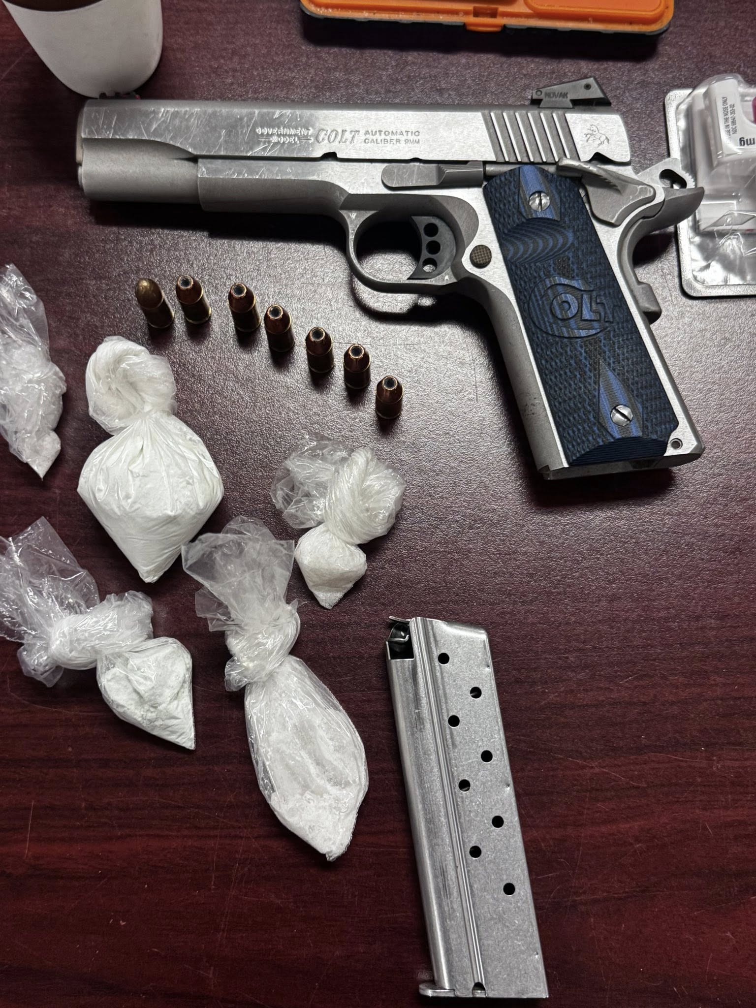 Silver handgun with bullets, magazine, and several small plastic bags containing white powder, all placed on a dark wooden surface.