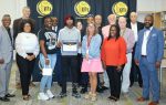 A group of people pose indoors with a young student holding a certificate, standing in front of a Marlboro County School District backdrop.