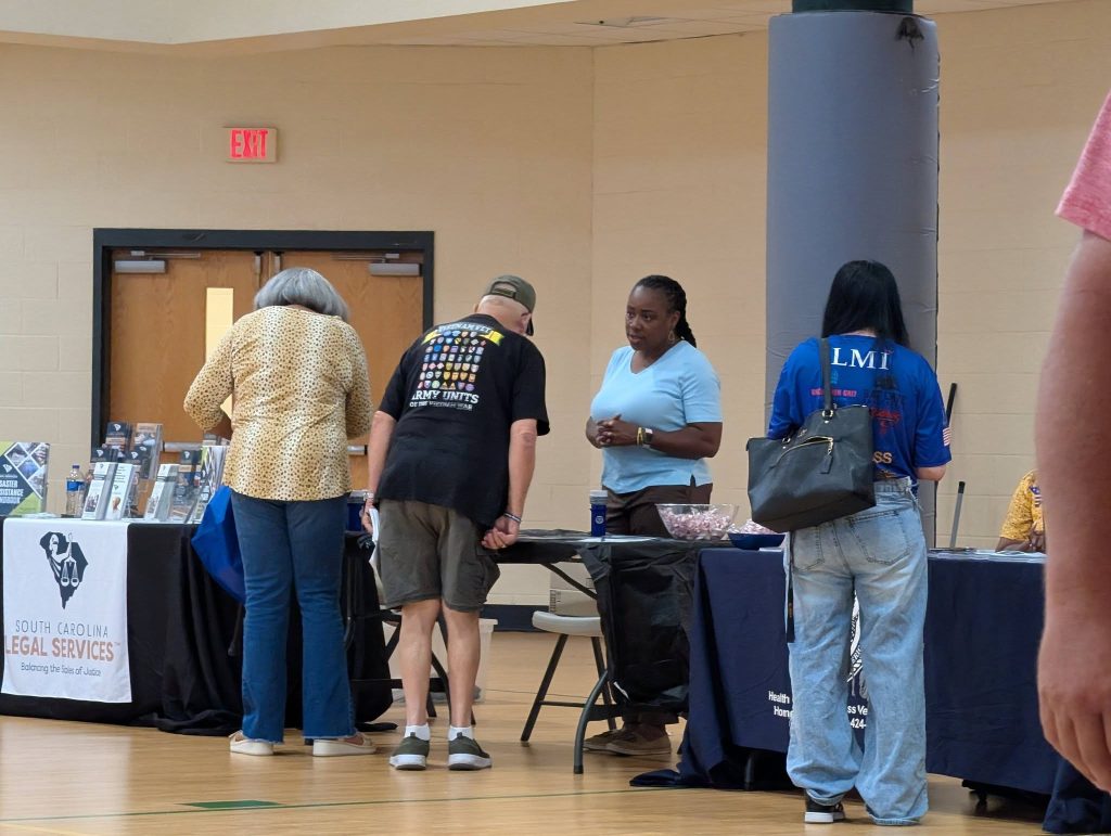 People standing and talking at tables inside a gymnasium during an indoor community event.