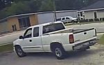 A white pickup truck parked on a street near a building with trees and other vehicles in the background.