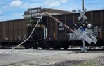 A freight train passes through a railroad crossing with a broken crossing gate arm hanging down.