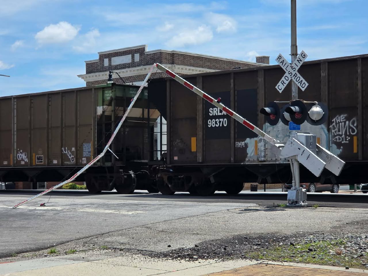 A freight train passes through a railroad crossing with a broken crossing gate arm hanging down.
