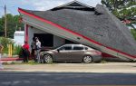 Collapsed building roof on top of a parked car, with several people standing nearby on the sidewalk, observing the damage.