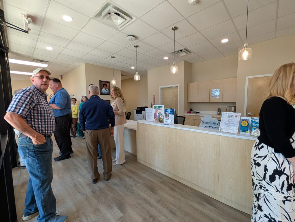 People standing and conversing inside a modern office or clinic lobby with a reception counter and informational flyers displayed.