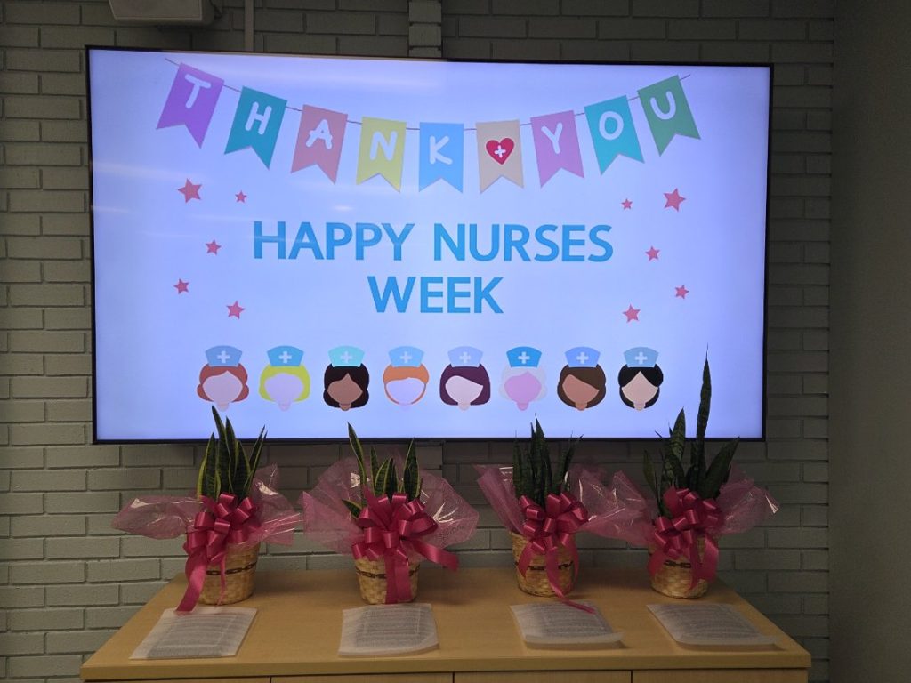 screen displays "Happy Nurses Week" with thank you banners, nurse icons, and stars. Four potted plants with pink ribbons sit on a table below.