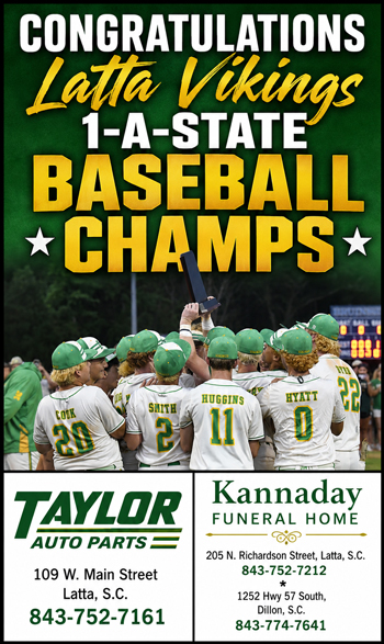 A baseball team celebrates on the field under a sign that reads "1A-State Baseball Champs," with players facing away, wearing green and white uniforms.