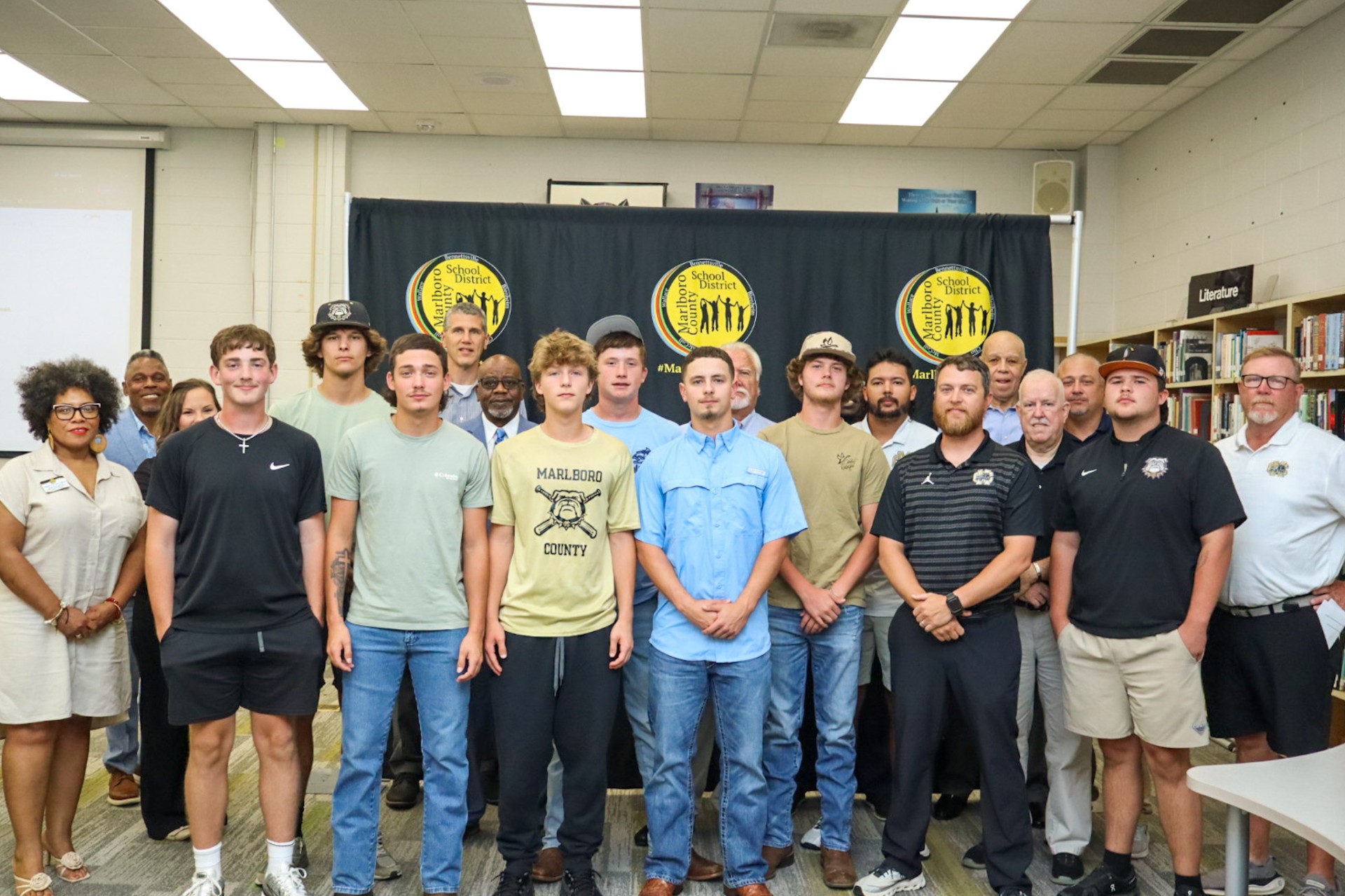 A group of men pose for a group photo indoors in front of a black and yellow banner.