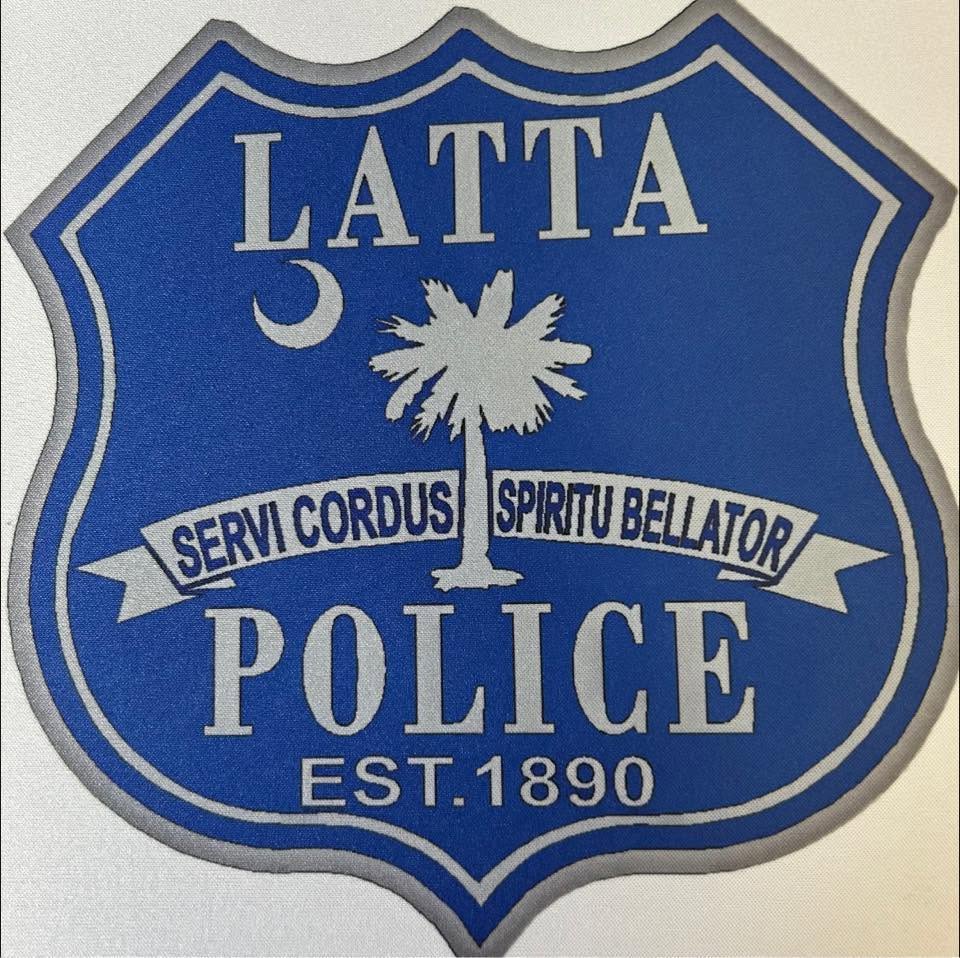 Blue Latta Police badge with a crescent, palmetto tree, Latin motto "Servi Cordus Spiritu Bellator," and "EST. 1890" at the bottom.