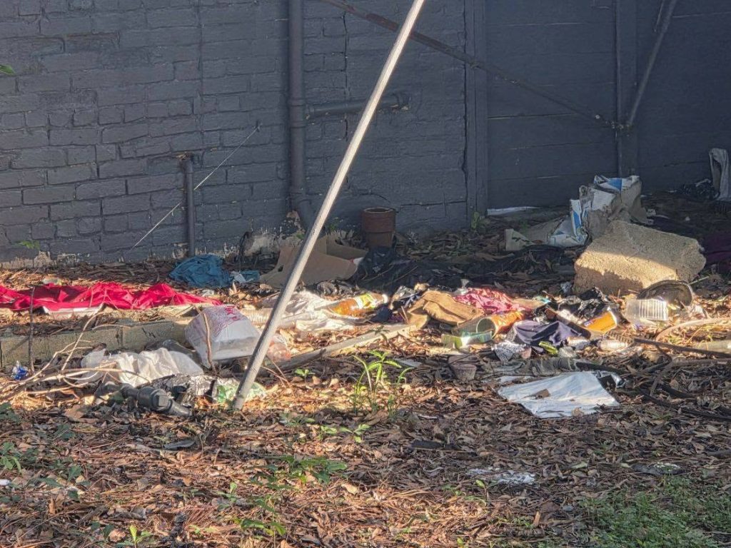 Trash and discarded items scattered on the ground outside, next to a gray brick wall and concrete steps.