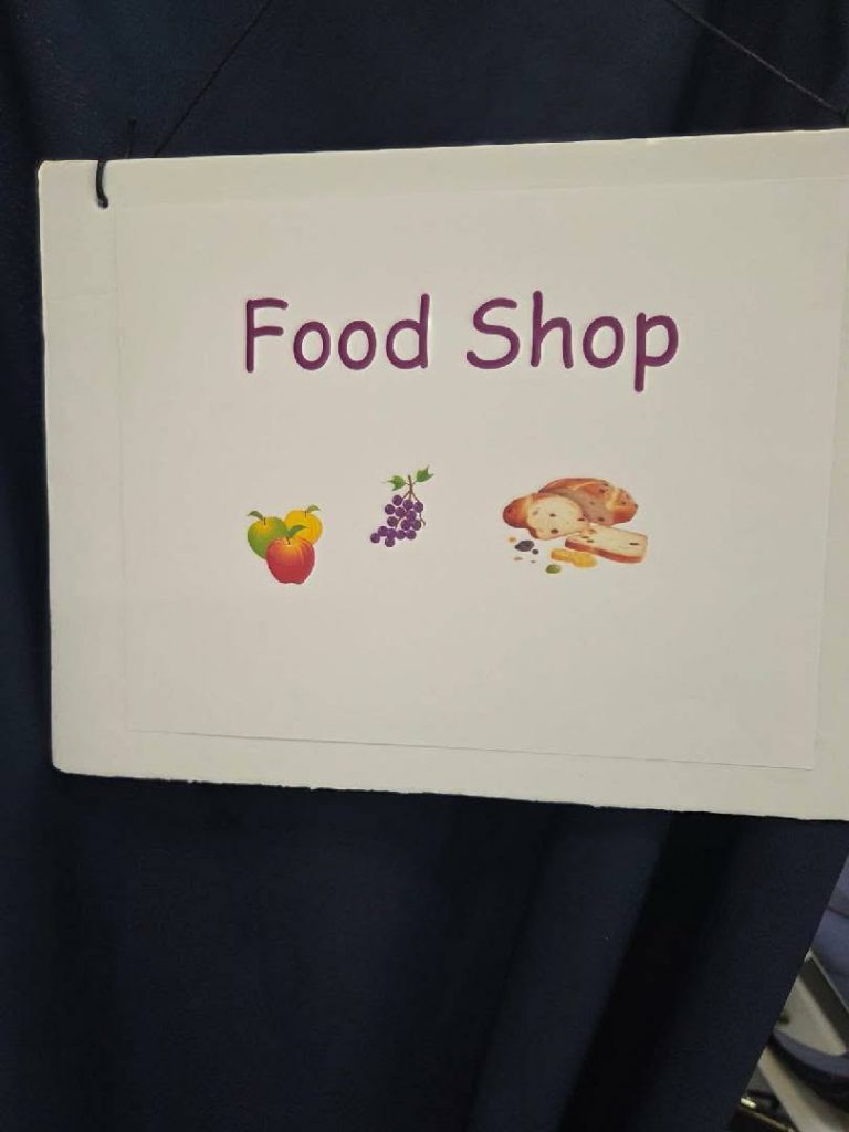 A sign reads "Food Shop" with illustrations of a fruit, grapes, and bread on a white background.