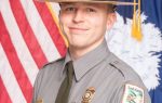 A South Carolina State Park ranger in uniform stands in front of the American and South Carolina flags, smiling for an official portrait.